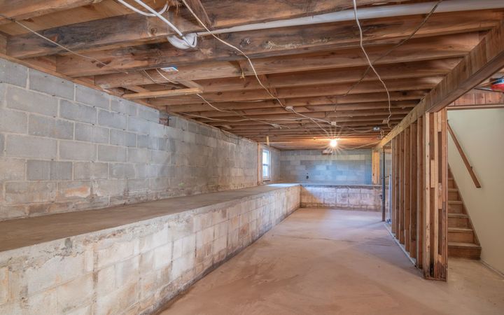 Unfinished basement with block walls, open joists and a stair