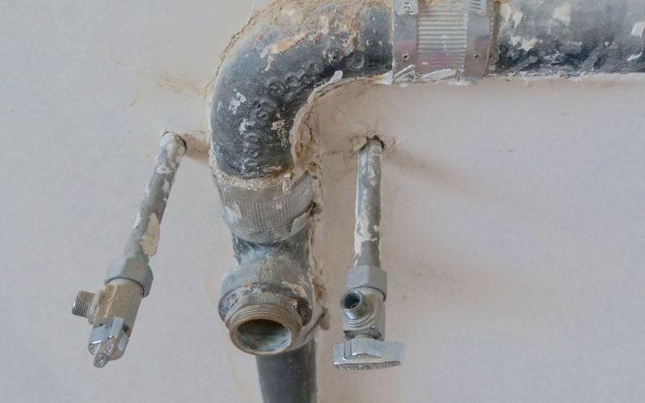 Old supply pipes and shutoff valves on a water-stained wall