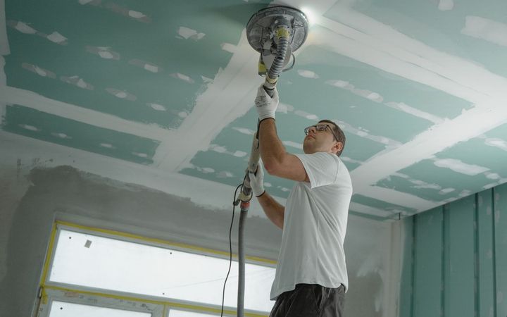 Finisher sanding a new drywall ceiling with a pole sander