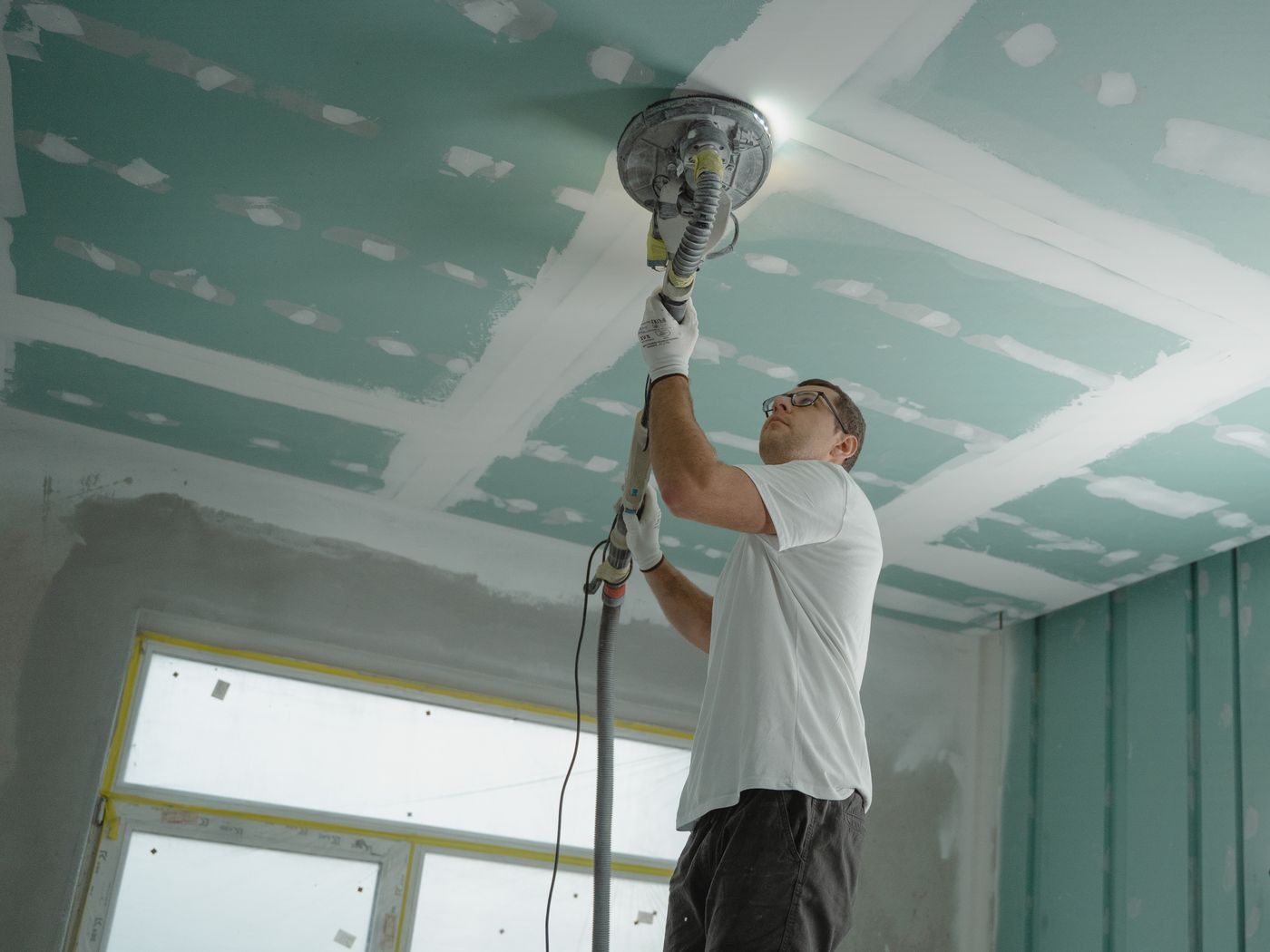 Finisher sanding a new drywall ceiling with a pole sander