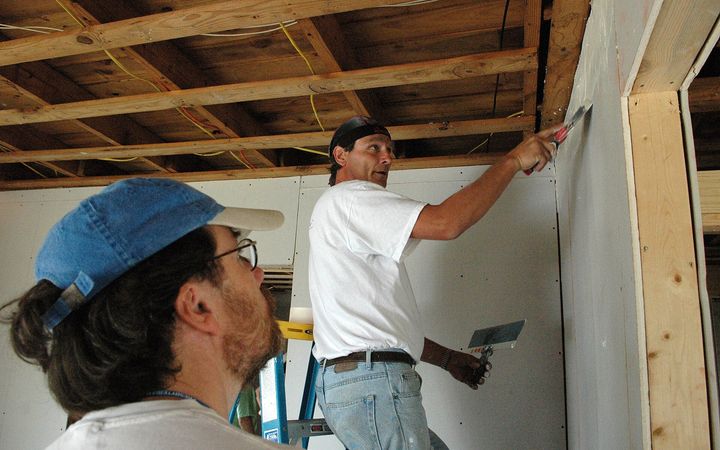 Two men finishing new drywall under open ceiling joists