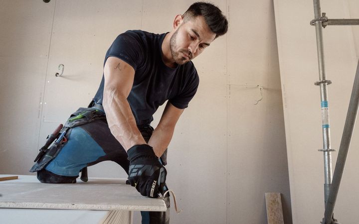 Drywall installer cutting a sheet of plasterboard to size