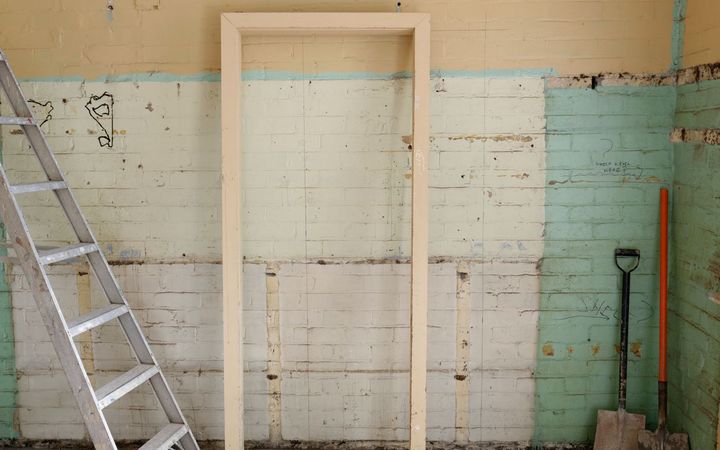 Room stripped back during a renovation, with a ladder and new door frame