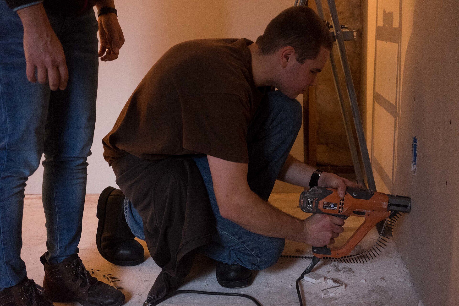 Man driving drywall screws low on a new wall with a screw gun