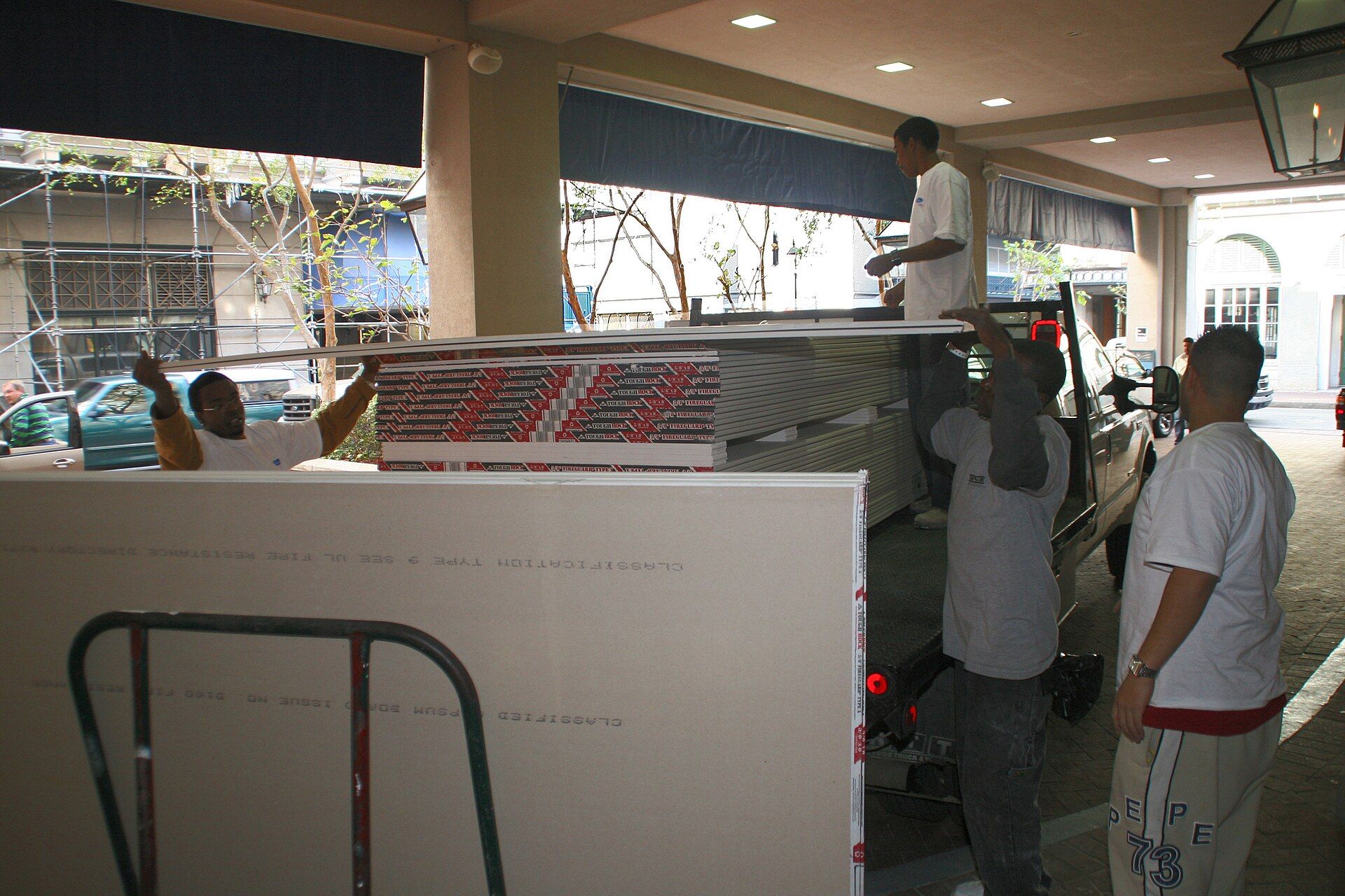 Workers wheeling sheets of new drywall into a gutted room