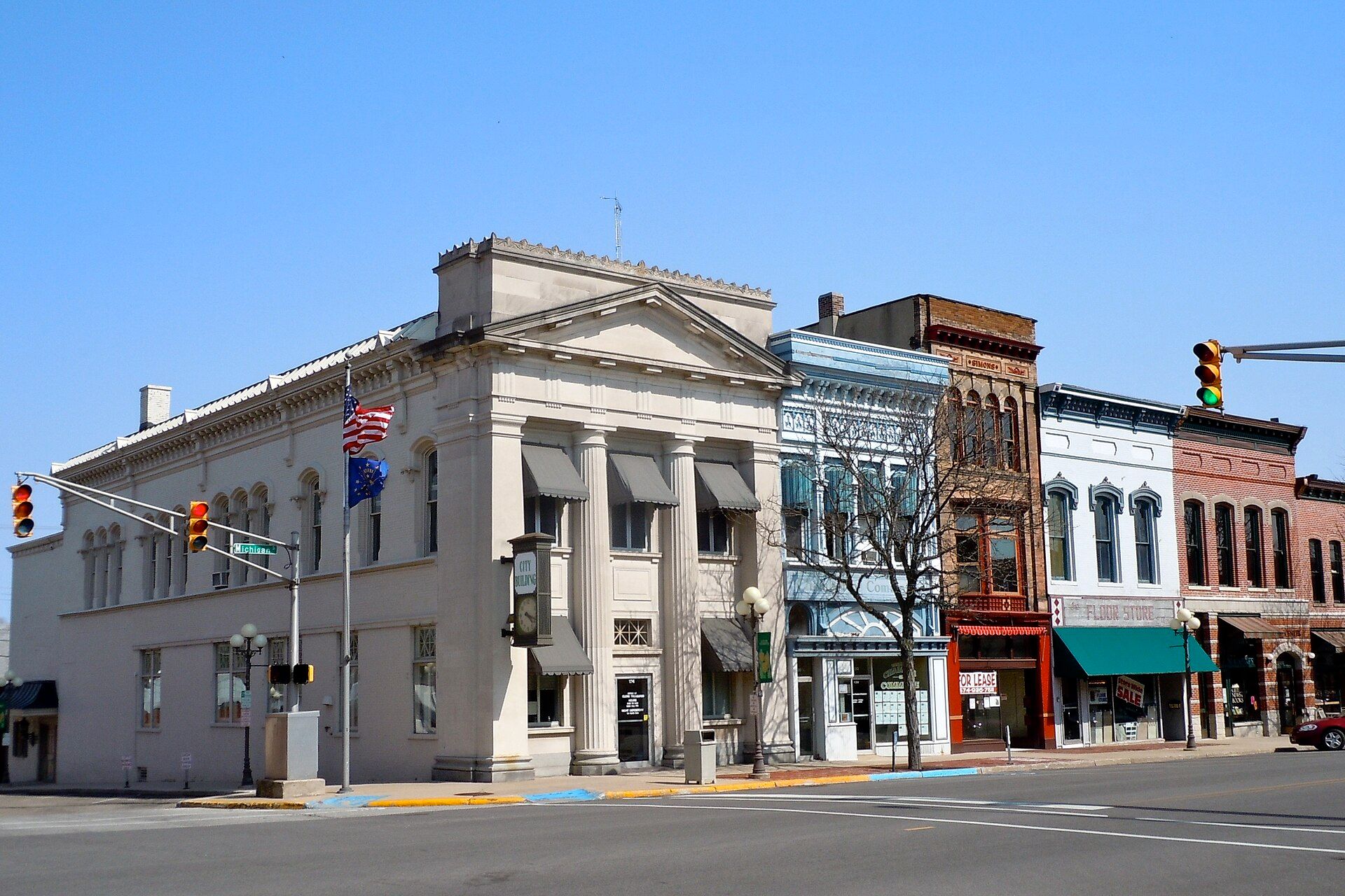 A columned stone building beside brick storefronts in downtown Plymouth, Indiana