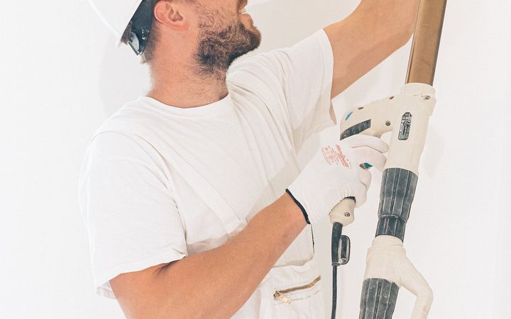 Finisher in a mask sanding a wall with a power sander