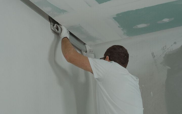 Drywall finisher mudding the seams where the wall meets the ceiling
