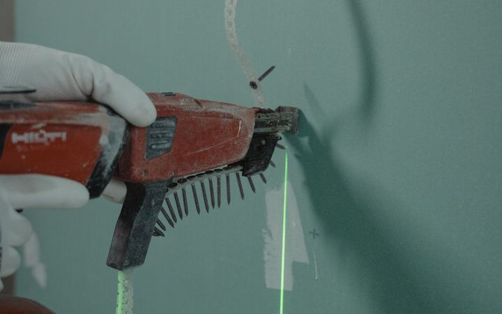 Screw gun fastening a drywall panel along a laser line