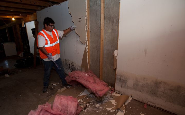 Worker tearing out a soaked wall, insulation piled on the floor