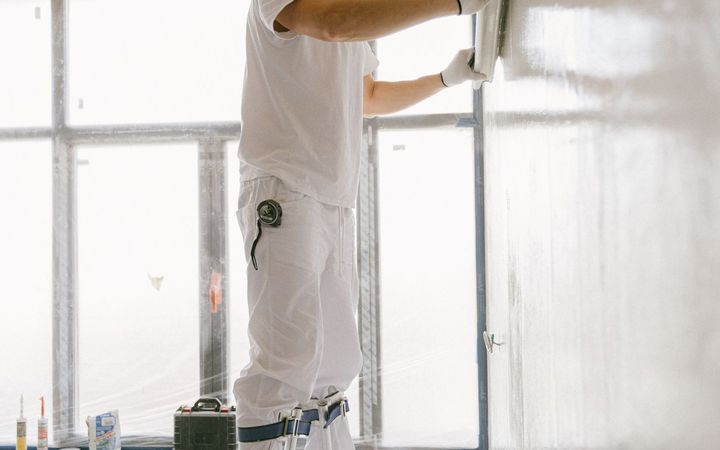 Finisher skim-coating a wall beside a bright window