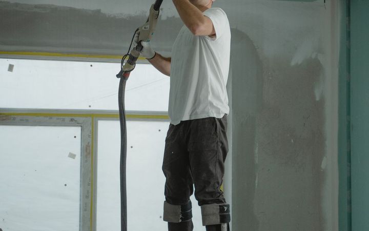 Worker on drywall stilts sanding a ceiling smooth