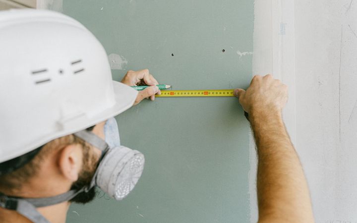 Installer in a respirator measuring a drywall panel