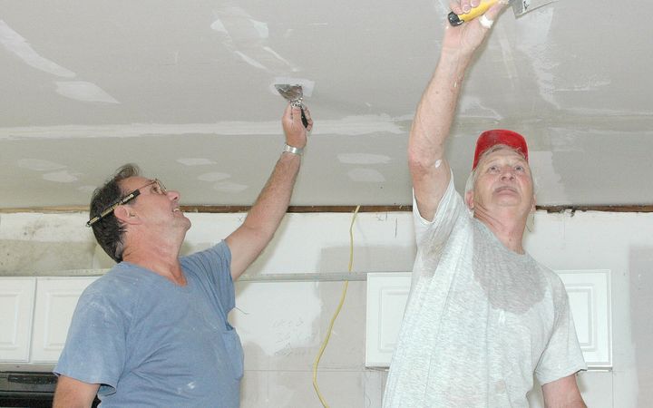 Two men taping and smoothing a drywall ceiling