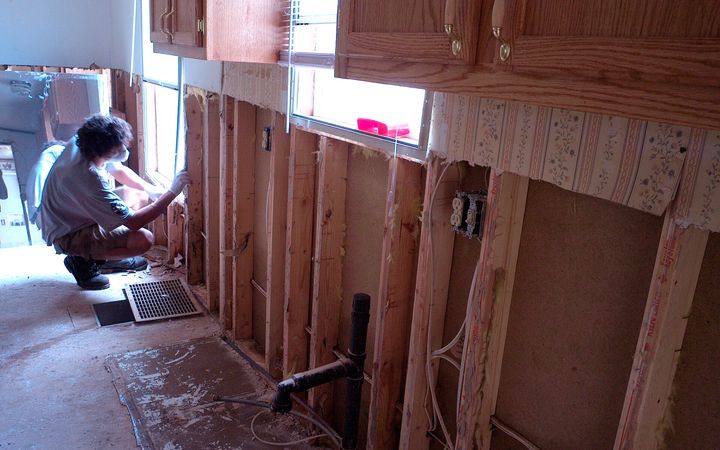 Kitchen wall opened to the studs, a worker kneeling at the framing